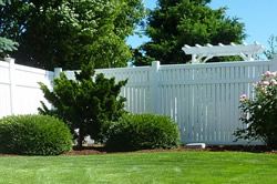 Photo of a tall white fence enclosing a nicely manicured lawn and shrubs.